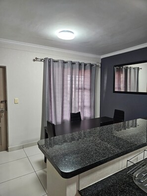 A modern kitchen with a granite countertop, a dining area with chairs, and a large mirror on the wall. - Sandton Westpoint Luxury Apartments 176 (Sandton)