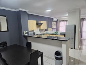 A modern kitchen with a central island, a dining table with chairs, and a trash bin. - Sandton Westpoint Luxury Apartments 176 (Sandton)