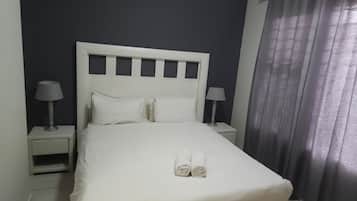 Una habitación de hotel con una cama, dos mesitas de noche y una cortina.