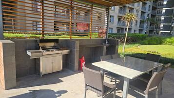 Un patio al aire libre con una parrilla, asientos y vistas a un edificio residencial.