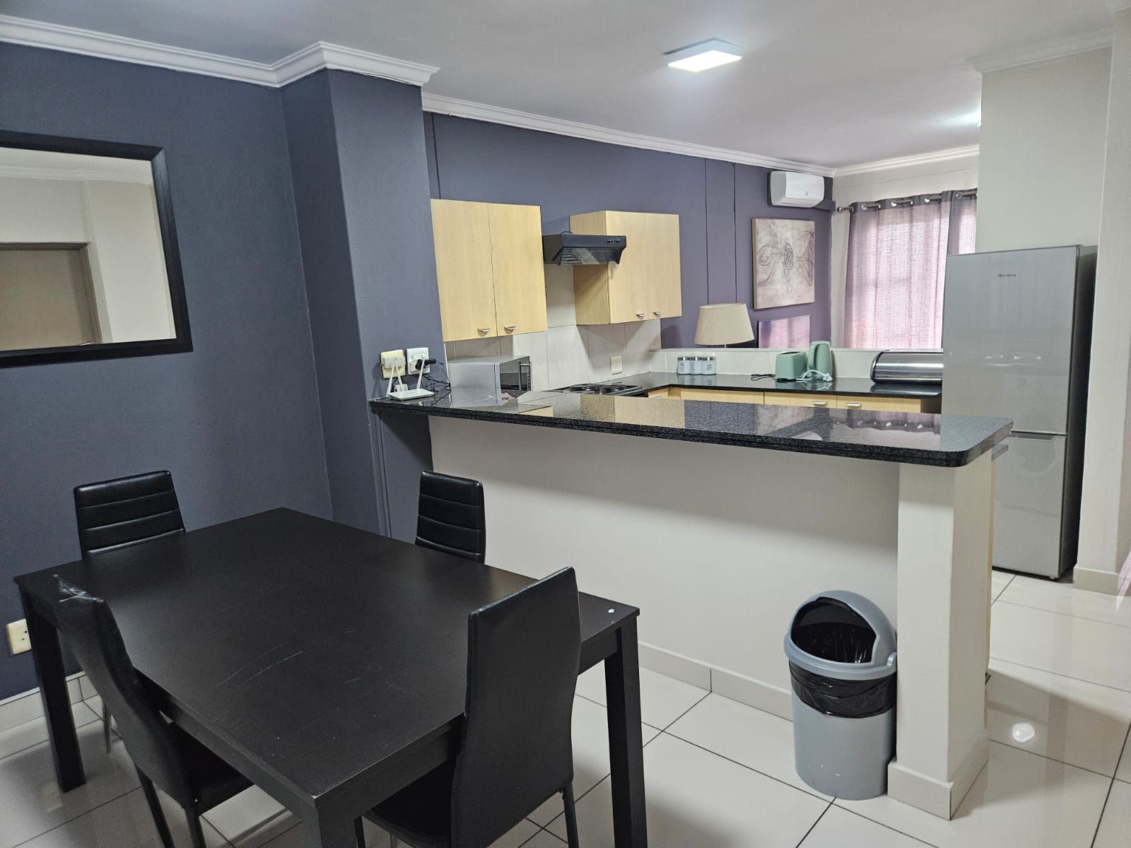 Una cocina compacta con comedor, un cubo de basura y un refrigerador.