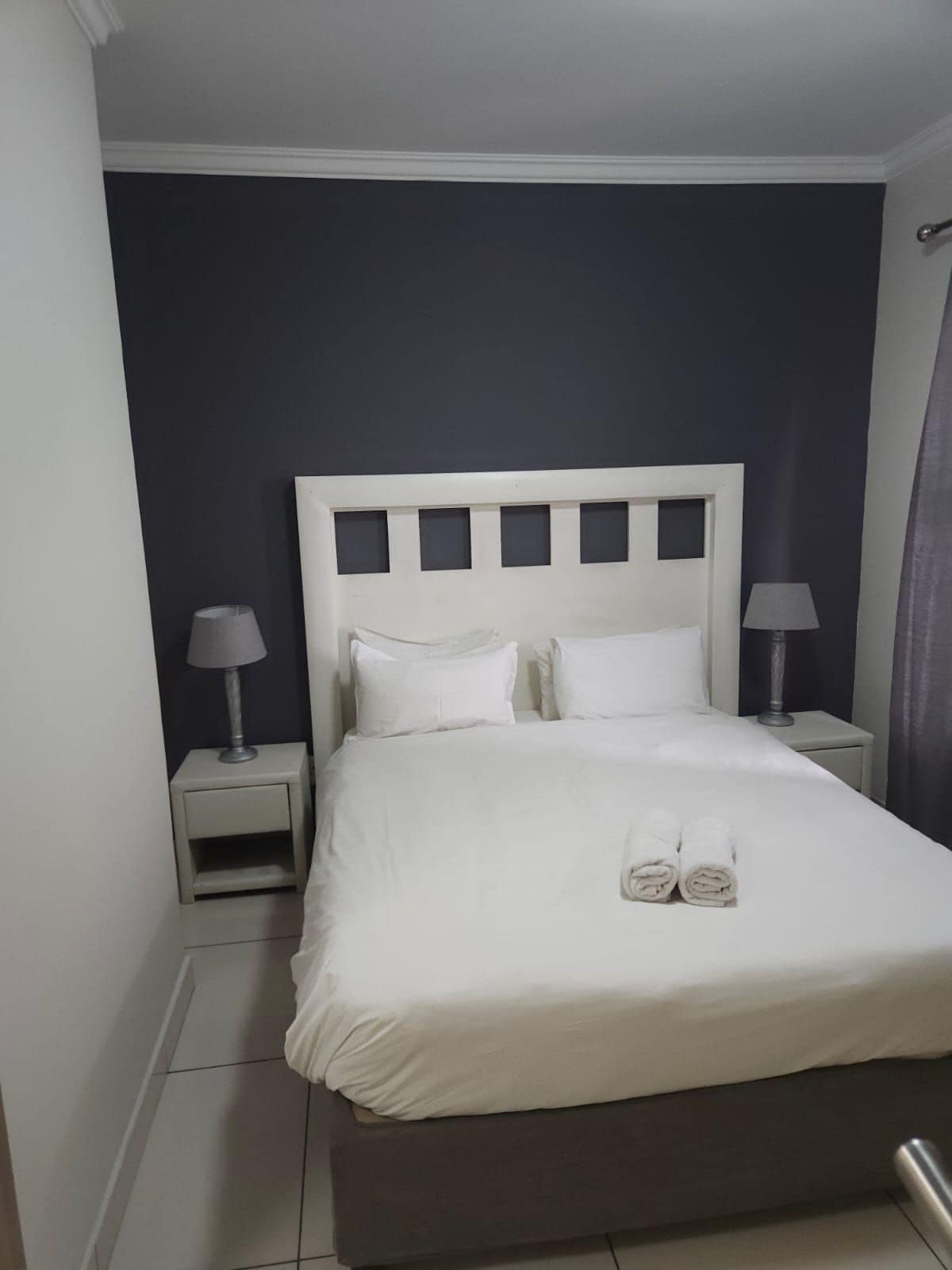 Una habitación de hotel con una cama, dos mesitas de noche con lámparas y una cortina.