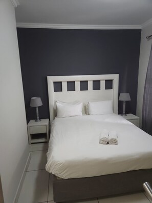 A hotel room with a bed, two bedside tables with lamps, and a curtain. - Sandton Westpoint Luxury Apartments 176 (Sandton)