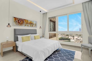 A modern bedroom with a large bed, a nightstand, a bedside table, a chair, a window with a city view, and a ceiling light. - 2 Bed Apt Palm Views, Marina & Atlantis Panorama (Dubai)