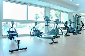 A gym with various exercise machines, large windows, and a view of a pool. - 2 Bed Apt Palm Views, Marina & Atlantis Panorama (Dubai)