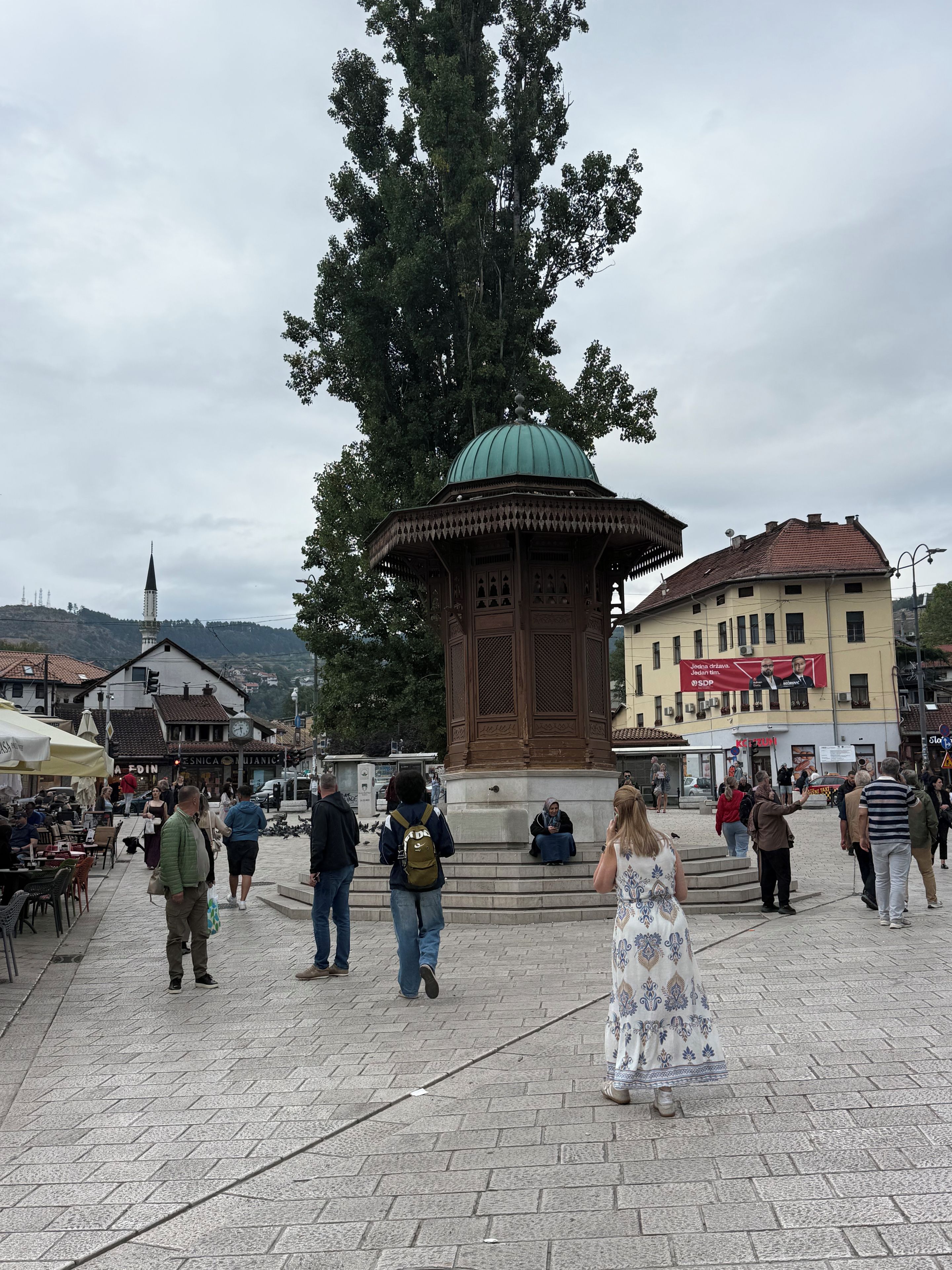 A public square with a central gazebo, surrounding buildings, and people walking.