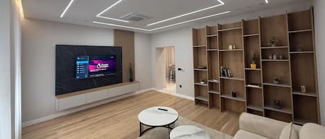 Una sala de estar moderna con un televisor de pantalla plana montado en la pared, pisos de madera, un sofá, dos mesas redondas y estanterías empotradas de madera.