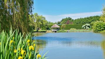 A tranquil pond with a gazebo, lush greenery, and a weeping willow.
