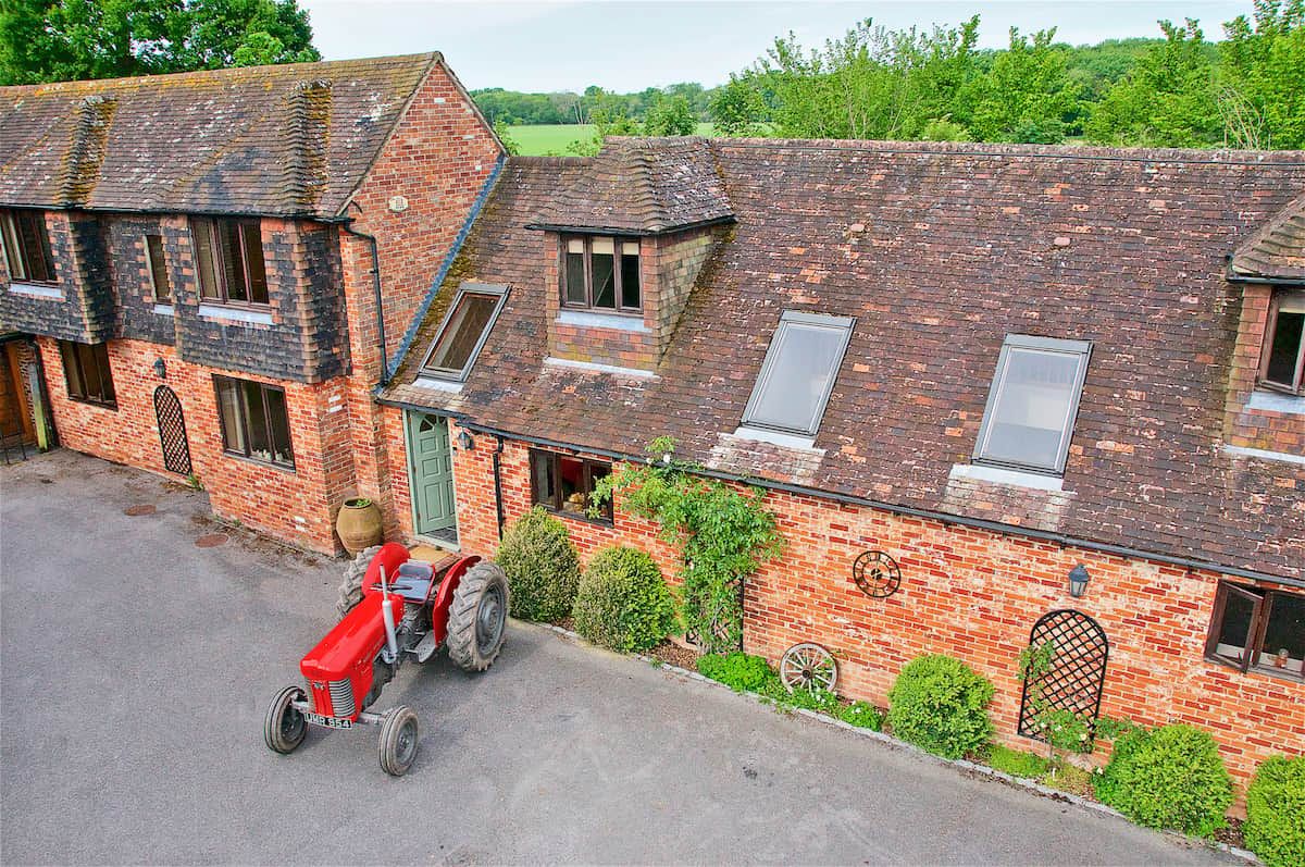 A red tractor parked in front of a brick building with multiple windows and a green door.