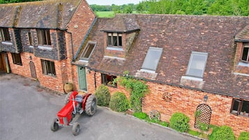 A red tractor parked in front of a brick building with multiple windows and a green door.