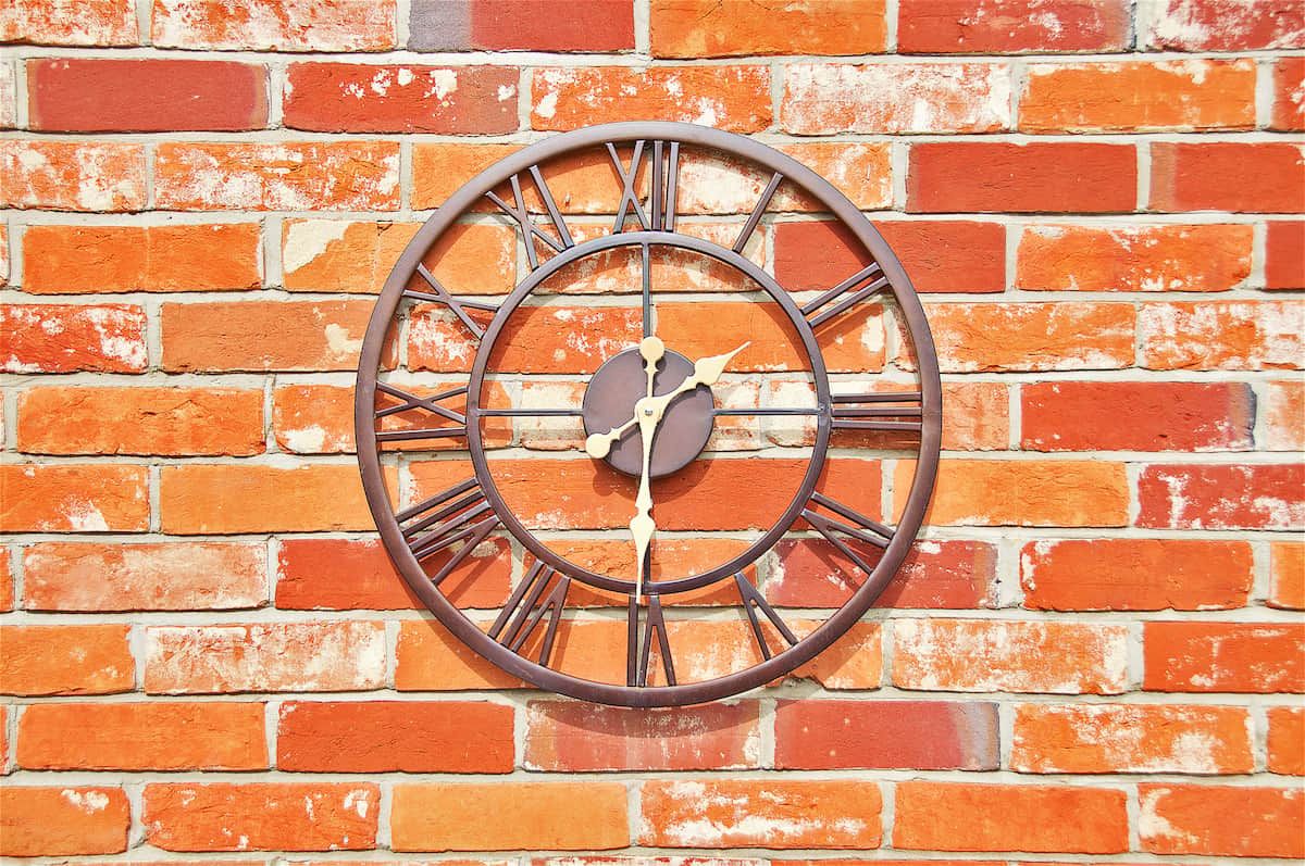 Un reloj de pared redondo con números romanos montado sobre una pared de ladrillo.