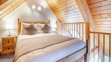 Une chambre avec un plafond en bois, un lit avec une literie blanche, une table de chevet et une balustrade en bois.