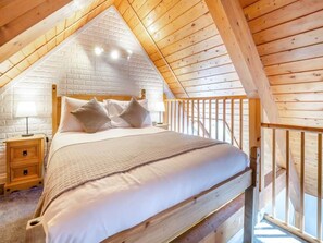 A bedroom with a wooden ceiling, a bed with white bedding, a nightstand, and a wooden railing. - Superior Chalet 2 at Northlands Farm – Near Goodwood (Chichester)