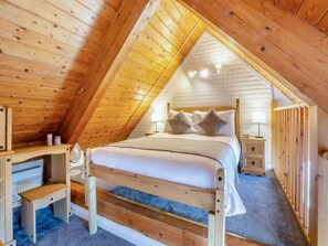 A bedroom with a wooden sloped ceiling, a bed with pillows, a bedside table, and a lamp. - Superior Chalet 2 at Northlands Farm – Near Goodwood (Chichester)