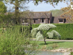 A building with a brick facade, a large tree with white blossoms in front, and a well-maintained hedge. - Superior Chalet 2 at Northlands Farm – Near Goodwood (Chichester)