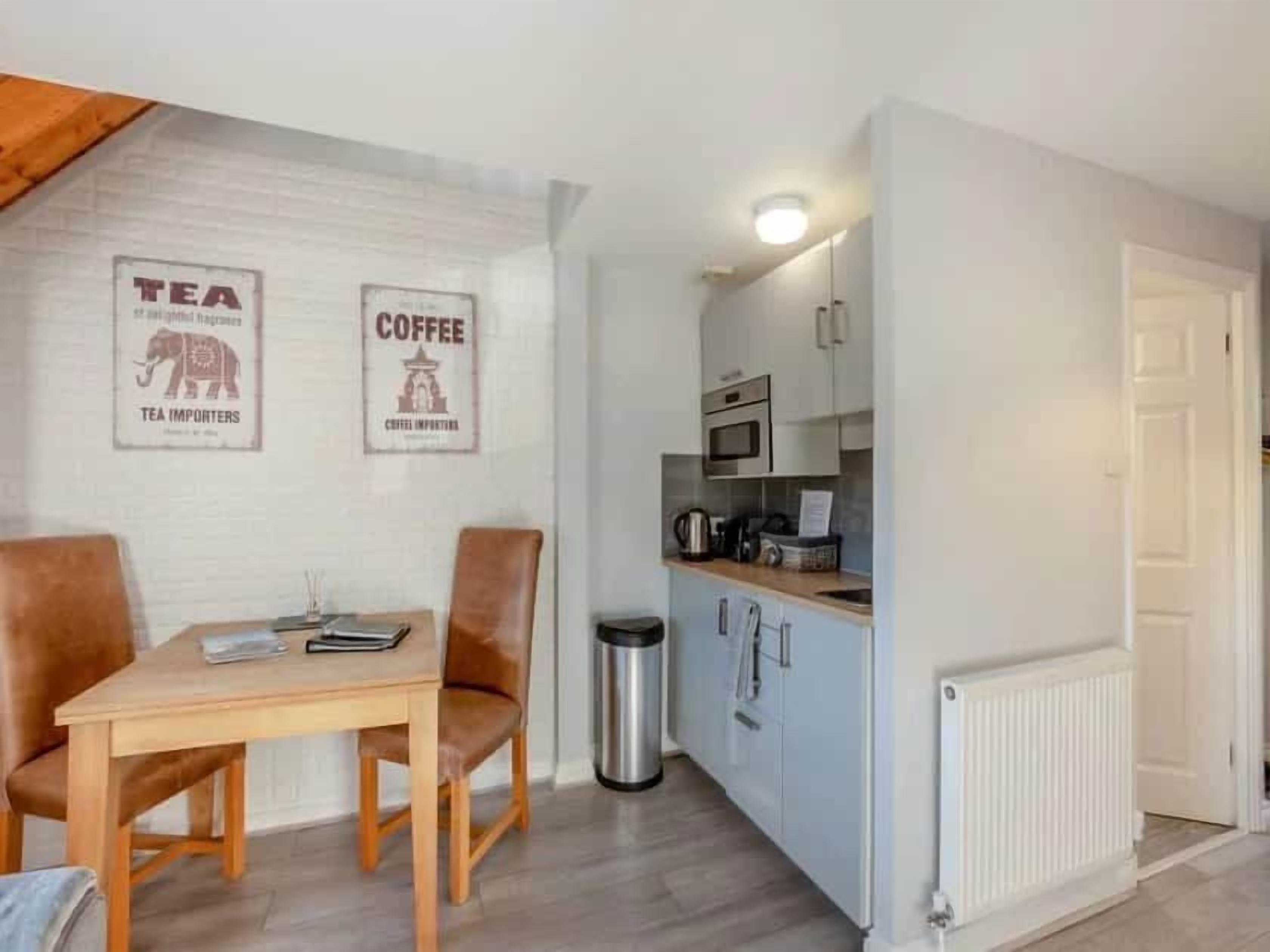 A compact kitchen with a dining area, featuring a table, chairs, and a trash bin.