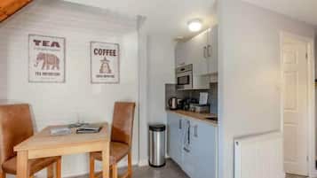 A compact kitchen with a dining area, featuring a table, chairs, and a trash bin.
