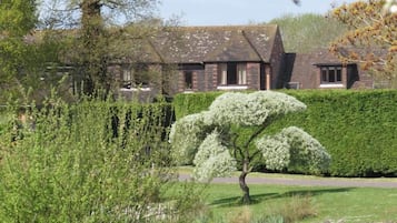 A building with a brick facade, a large tree with white blossoms in front, and a well-maintained hedge.