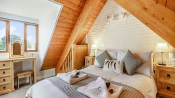 A bedroom with a sloped ceiling, a bed with pillows, a bedside table, and a desk with drawers.