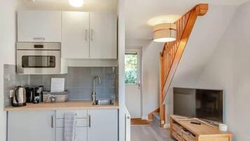 A modern kitchen with a microwave, stove, and sink, a wooden dining table, and a TV in a living area.