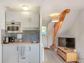 A modern kitchen with a microwave, stove, and sink, a wooden dining table, and a TV in a living area.