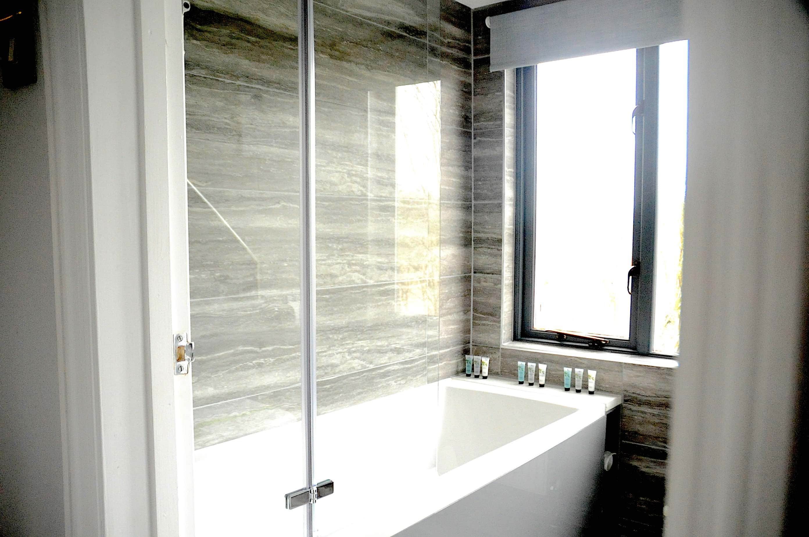 Un bagno con box doccia in vetro, una vasca da bagno ampia e una finestra che permette l'ingresso di luce naturale.