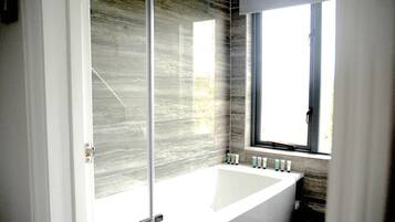 Un bagno con box doccia in vetro, una vasca da bagno ampia e una finestra che permette l'ingresso di luce naturale.