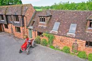 A red tractor parked in front of a brick building with multiple windows and a green door.