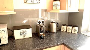 A kitchen with a bread maker, a kettle, and jars of biscuits, coffee, tea, and sugar on the counter.