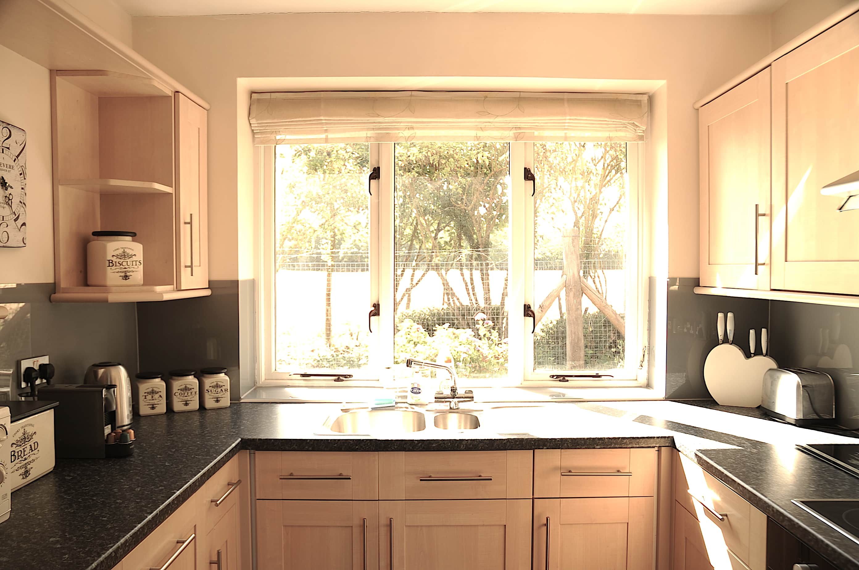 A kitchen with a large window, wooden cabinets, and a countertop with various appliances and jars.