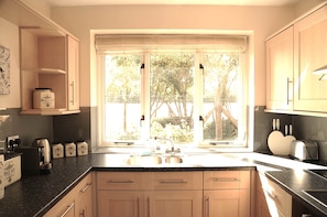 A kitchen with a large window, wooden cabinets, and a countertop with various appliances and jars.