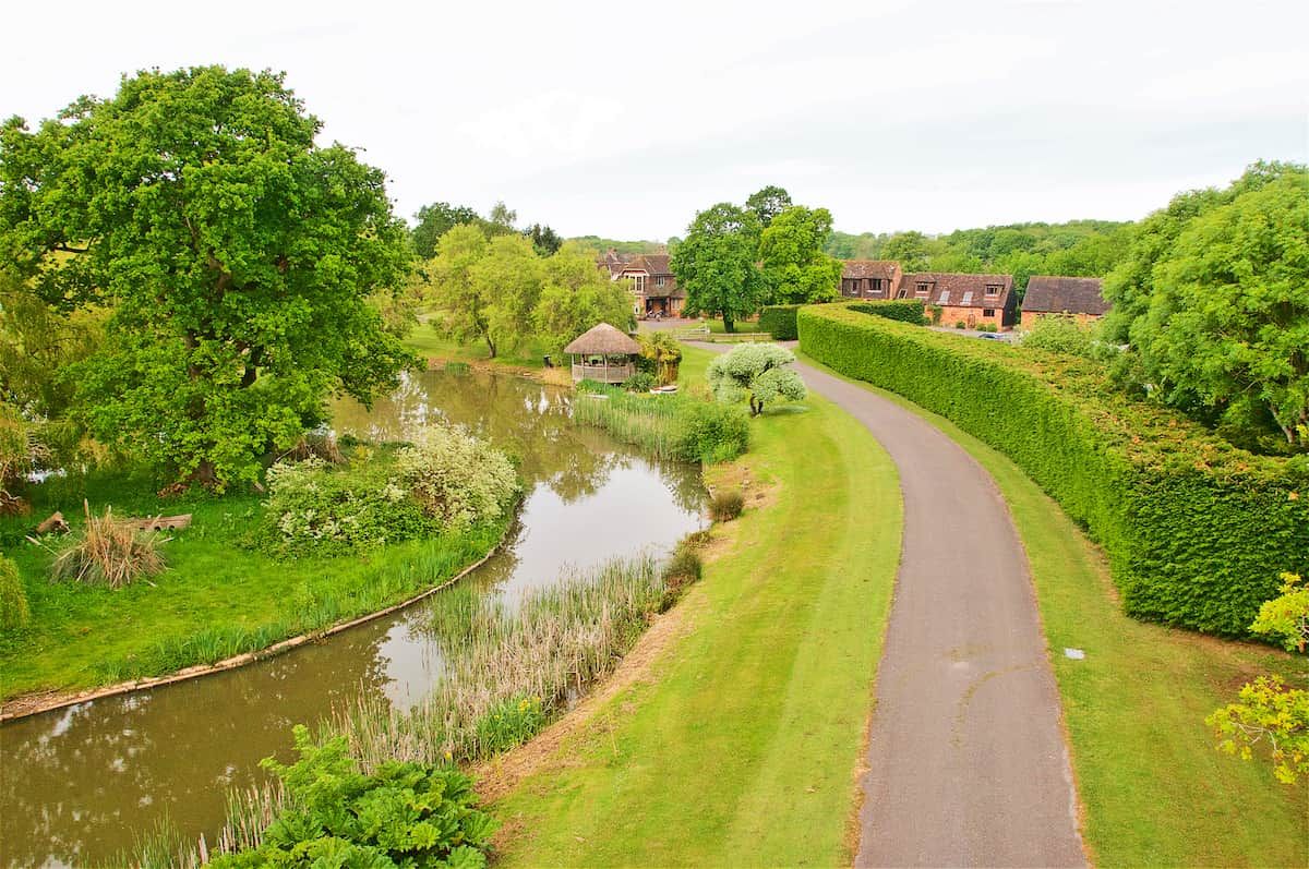 A rural landscape with a curved road, a pond, and houses with thatched roofs.