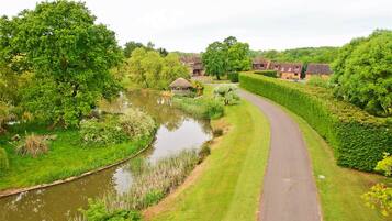 A rural landscape with a curved road, a pond, and houses with thatched roofs.