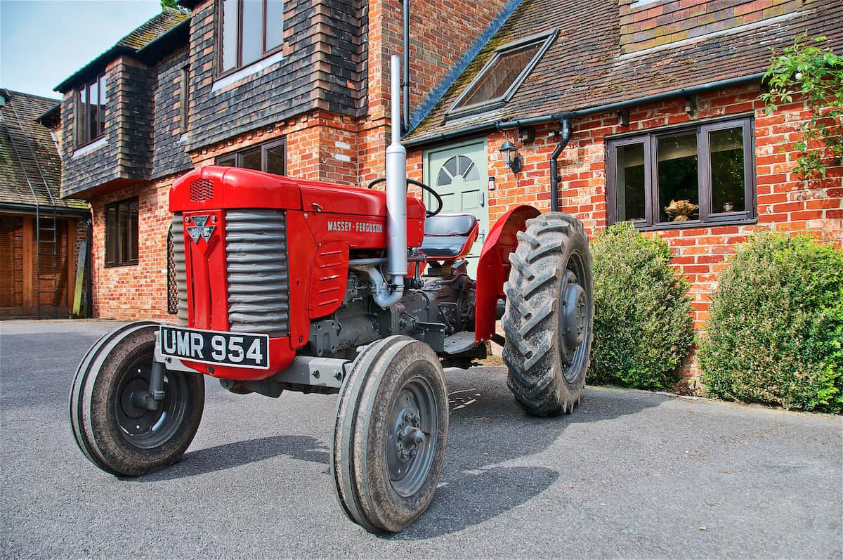 A red Massey-Ferguson tractor parked in front of a brick house with a visible license plate.