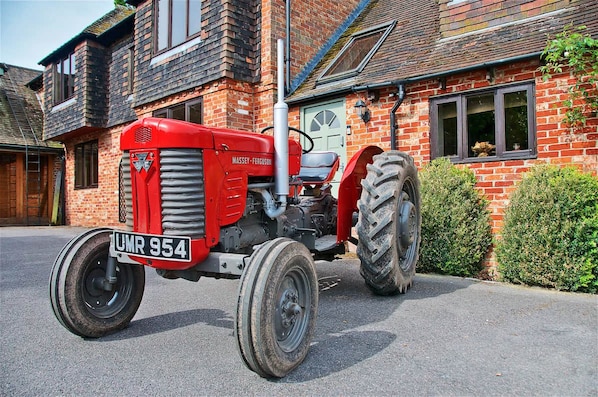 A red Massey-Ferguson tractor parked in front of a brick house with a visible license plate.