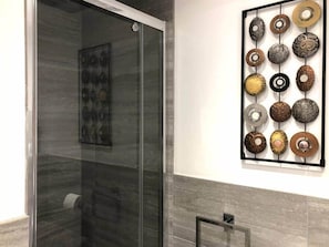 A bathroom with a glass shower enclosure and a wall-mounted art piece of circular objects.