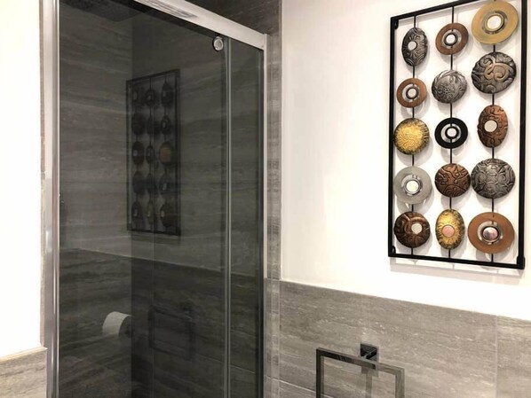 A bathroom with a glass shower enclosure and a wall-mounted art piece of circular objects.