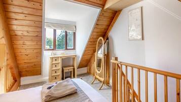 Une chambre avec un plafond en pente, des murs en bois, un lit, une commode, un miroir et une fenêtre.