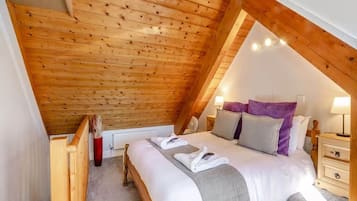 Une chambre à coucher avec un plafond en pente, un lit avec une literie blanche, une table de chevet et une commode.