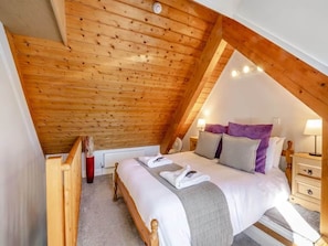 A bedroom with a sloped ceiling, a bed with white bedding, a bedside table, and a nightstand.