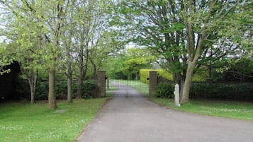 A paved driveway leading to a gated entrance surrounded by trees.