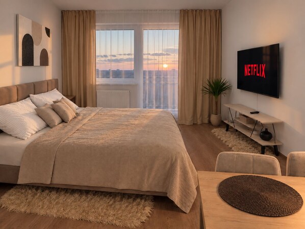 A modern hotel room with a large bed, a TV, and a view of the cityscape.