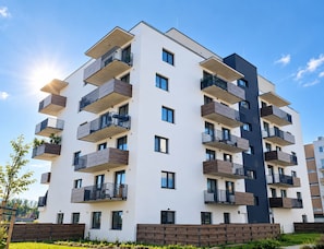 A multi-story residential building with balconies, a flat roof, and a clear sky.