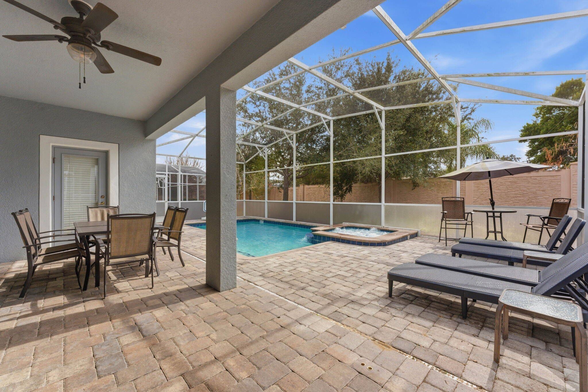 A covered outdoor area with a pool, lounge chairs, and a ceiling fan.