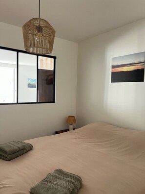 A bedroom with a bed, a bedside lamp, a hanging light fixture, a mirror, and a wall-mounted picture. - Charming apartment in the heart of the Morvan (Luzy)