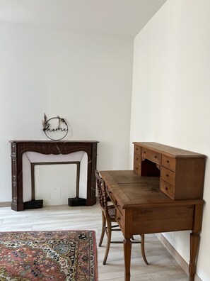 A room with a wooden desk and a chair, a small rug, and a wall-mounted sign. - Charming apartment in the heart of the Morvan (Luzy)