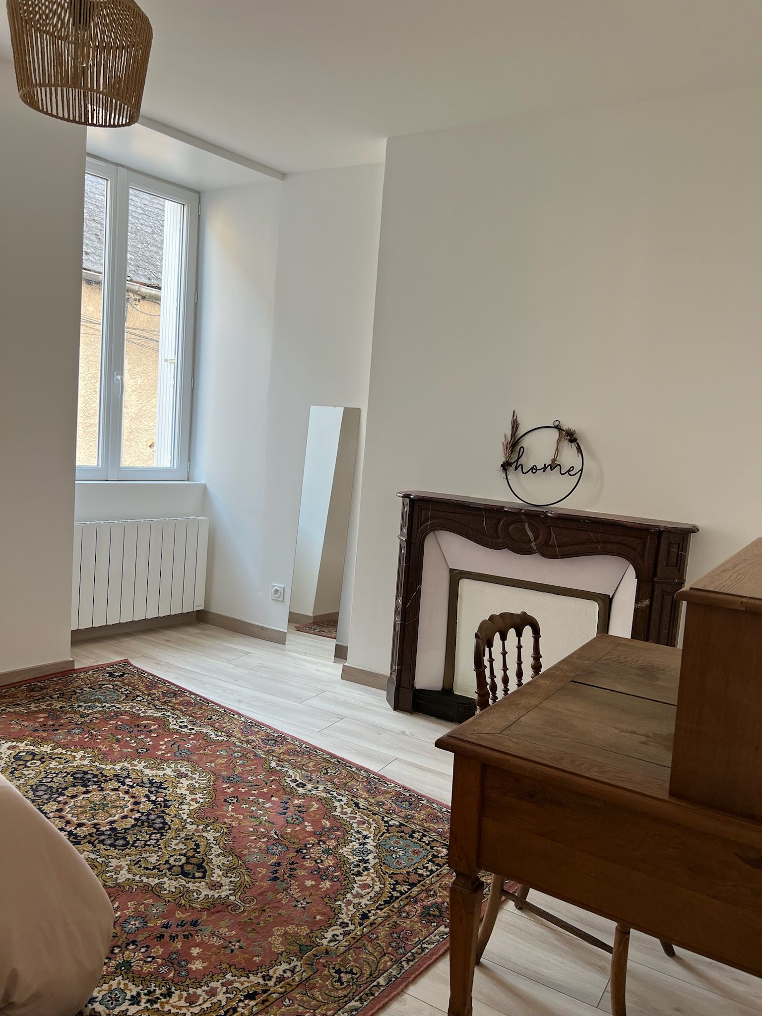 A room with a fireplace, a rug, a wooden table, and a window.