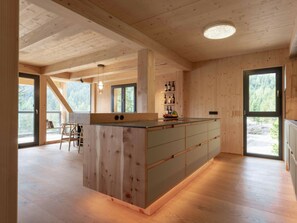 A spacious kitchen with wooden cabinetry, a central island, and a view of the outdoors through large windows. - Cabin in Turrach With Sauna and Balcony (Stadl-Predlitz)