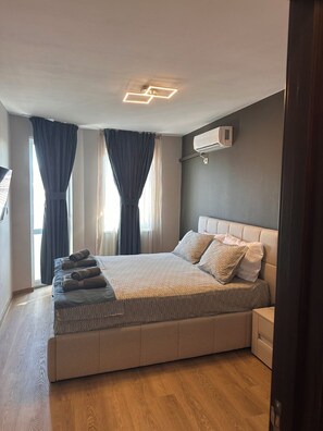 A modern bedroom with a large bed, a bedside table, an air conditioning unit, and a view of the outdoors through a window. - Cashmere Suite - Stylish Seaside Stay in Pomorie (Pomorie)