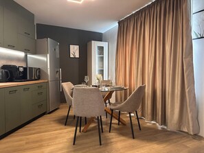 A modern kitchen with a dining area, featuring a coffee machine, refrigerator, and a table set for dining. - Cashmere Suite - Stylish Seaside Stay in Pomorie (Pomorie)